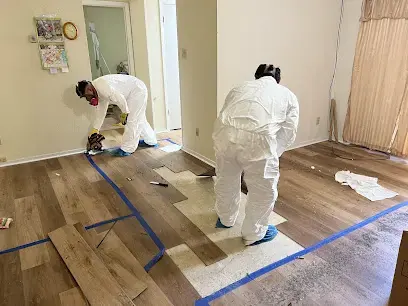 Restoration techs in protective suits removing wet flooring after a water loss